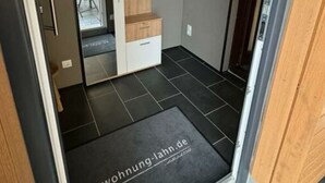 A modern interior with a dark floor, a wooden bench, a small shelf with a plant, and a door leading to another room. - Lovely Apartment Near the Water (Weilburg)