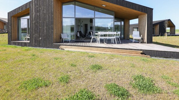 A modern house with large glass windows, a wooden deck, and outdoor seating. - Stylish Countryside Home (Wissenkerke)