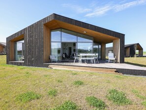 Une maison moderne dotée de grandes baies vitrées, d’une terrasse en bois et d’un espace salon extérieur.