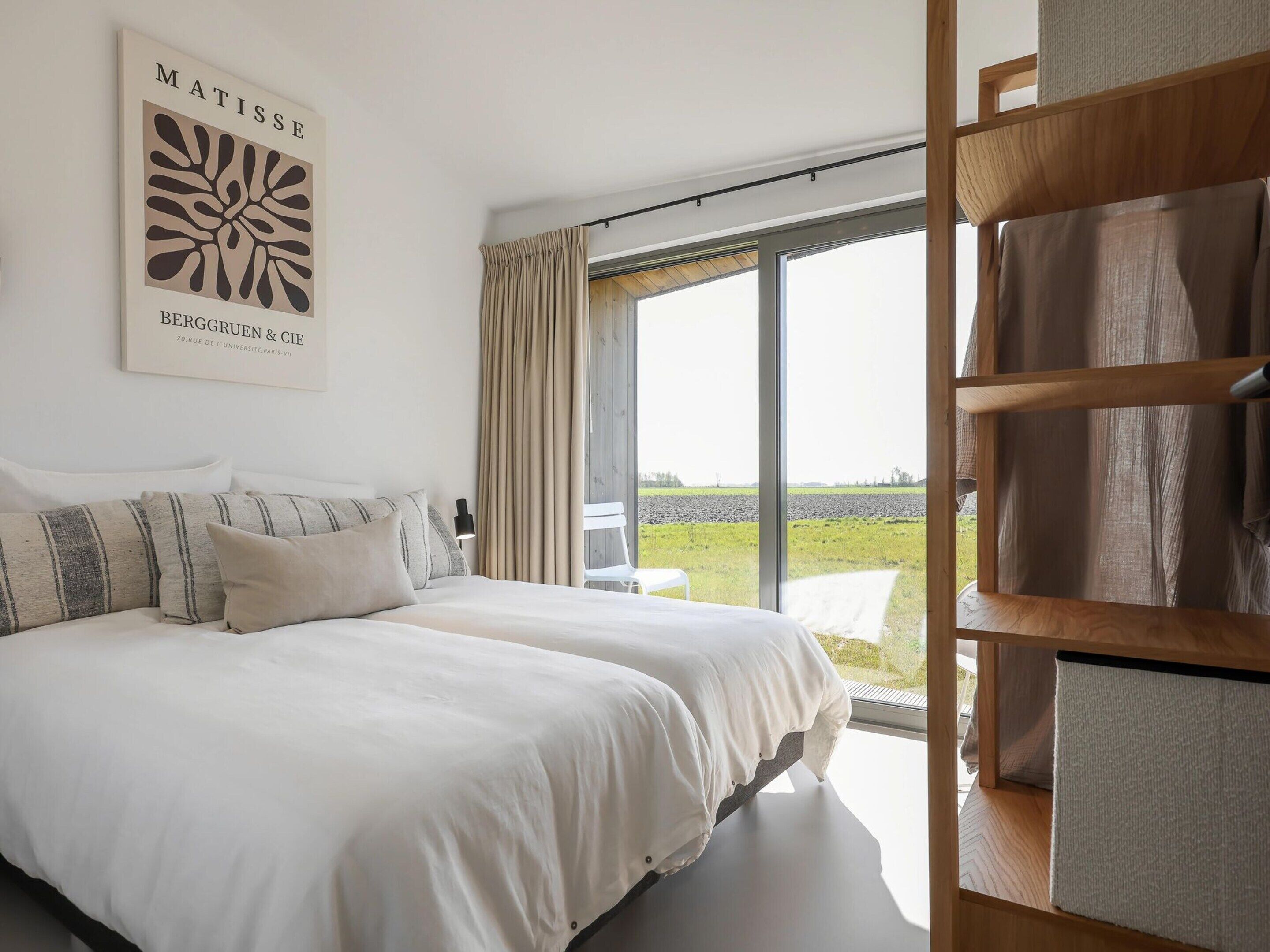 A bedroom with two beds, a large window, and a view of a field.