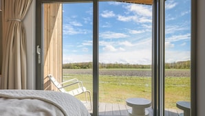 A bedroom with a large window, a bed, a chair, and a small table. - Stylish Countryside Home (Wissenkerke)
