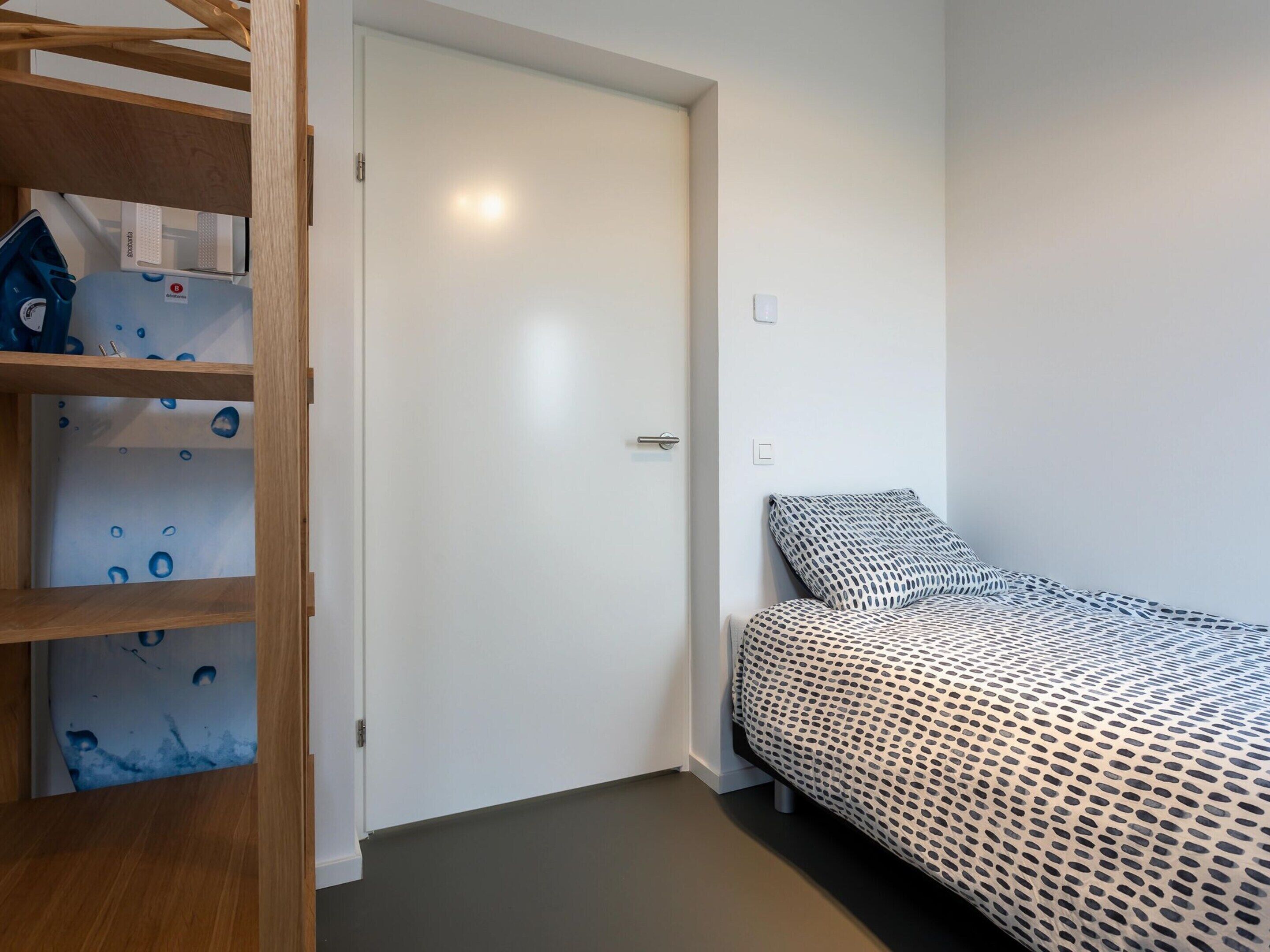 A bedroom with a bed, a wooden shelf unit, and a white door.