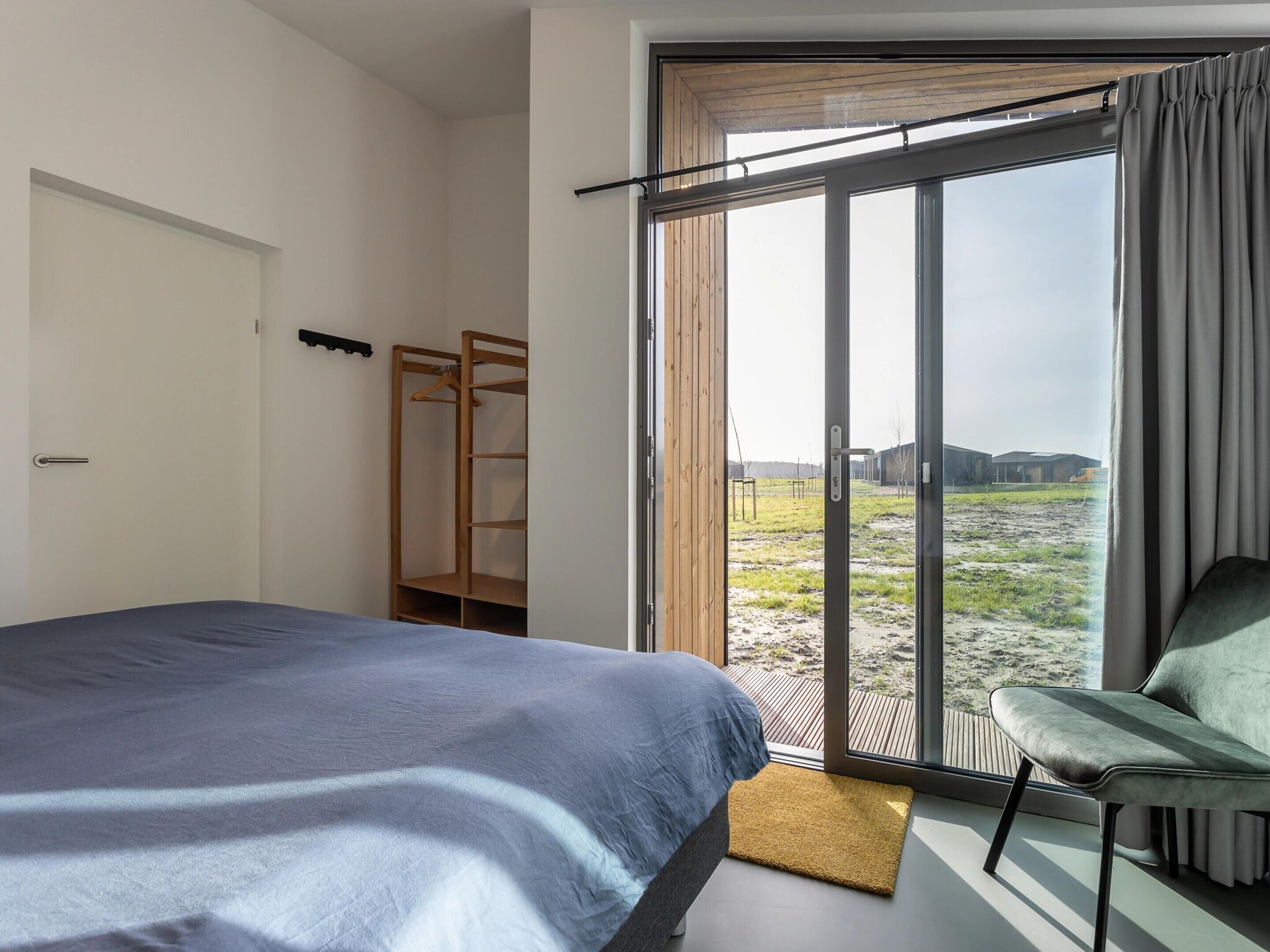 A bedroom with a bed, a chair, a wooden wardrobe, and a sliding glass door leading to an outdoor area.
