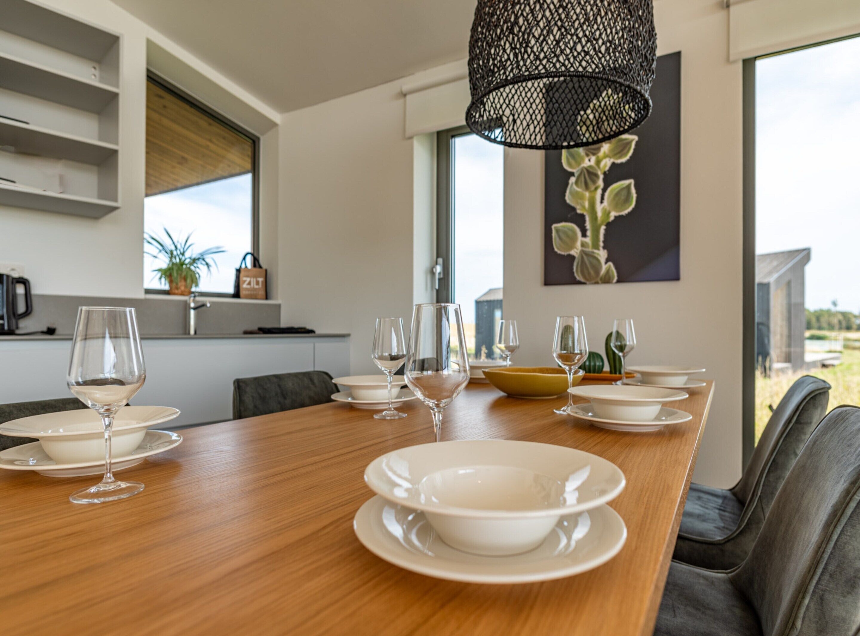 A modern dining area with a wooden table set for six, white plates, and wine glasses.
