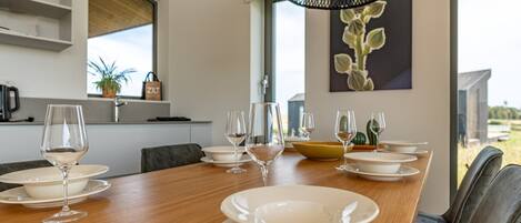 A modern dining area with a wooden table set for six, white plates, and wine glasses.