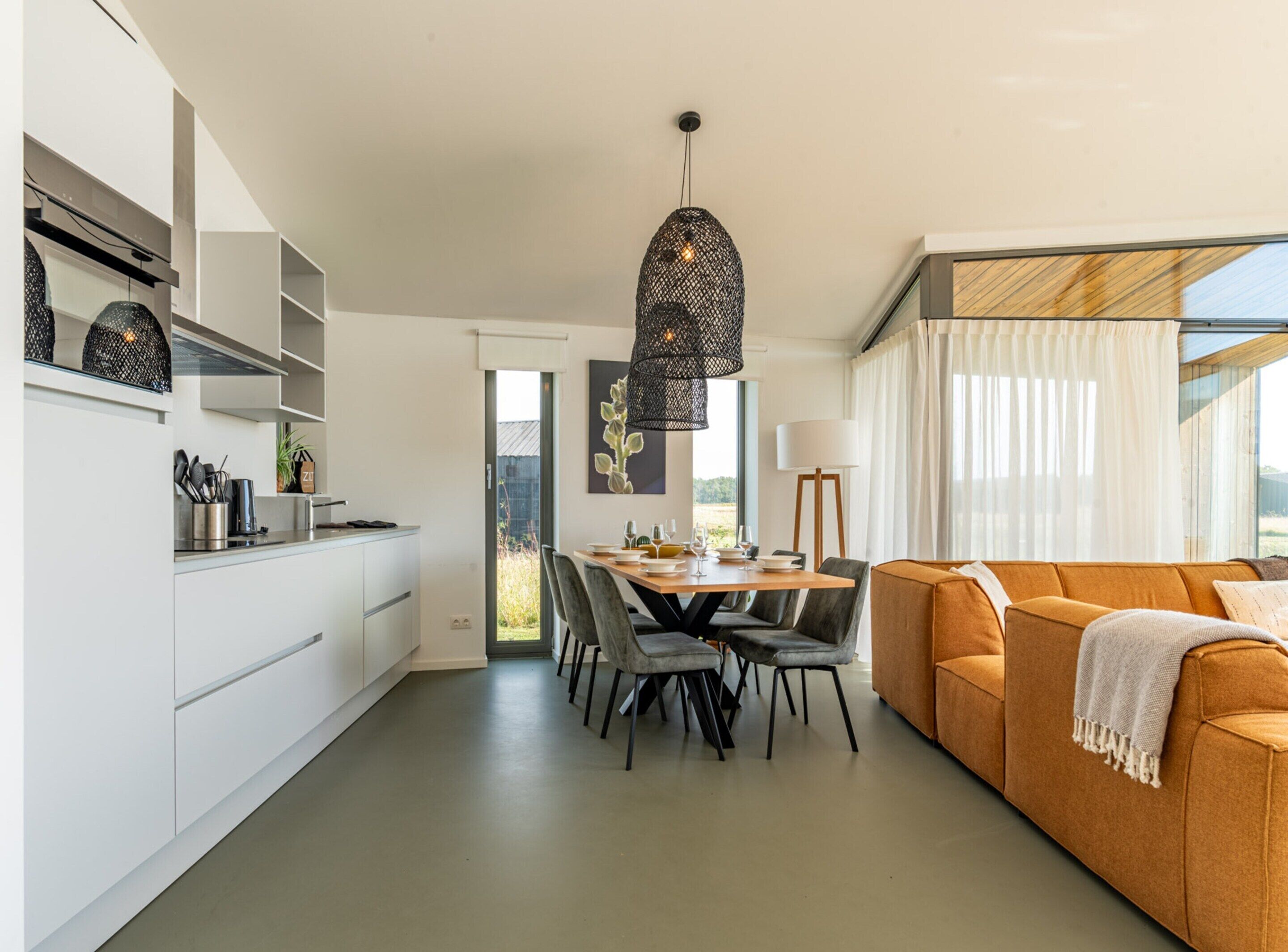 Una cocina moderna con armarios blancos, una zona de comedor con una mesa y sillas de madera, y un sofá naranja acogedor.
