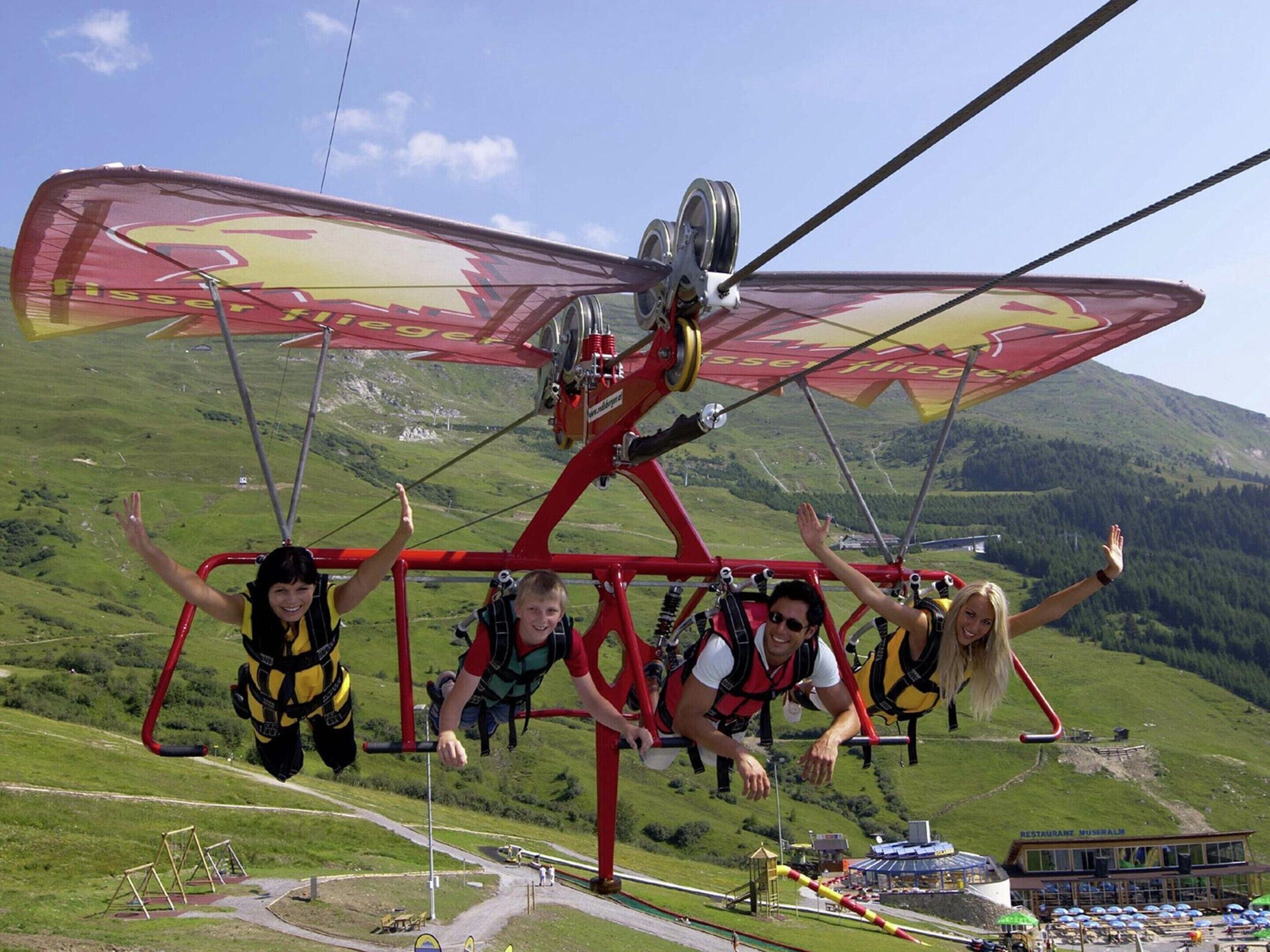 A group of people on a red cable car with a scenic mountain view in the background.