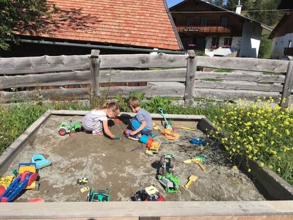Children playing with toy vehicles in a sandbox.