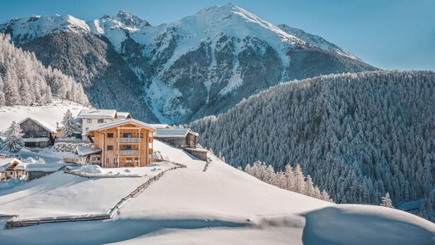 Eine verschneite Berglandschaft mit einer Holzhütte, die mehrere Balkone und eine Skipiste im Vordergrund zeigt.