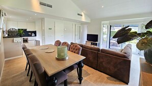 A modern living room with a dining table, brown sofa, and a TV. - Bamboo Holiday Home in Veluwe (Voorthuizen)