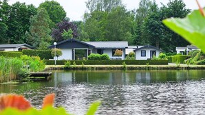 A row of modern, single-story houses with a pond in the foreground. - Bamboo Holiday Home in Veluwe (Voorthuizen)