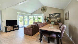A spacious living area with a large sectional sofa, a dining table, and a flat-screen TV. - Bamboo Holiday Home in Veluwe (Voorthuizen)
