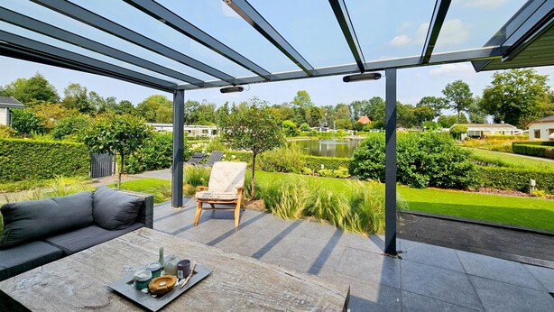 A covered patio with a view of a lake and manicured garden. - Bamboo Holiday Home in Veluwe (Voorthuizen)