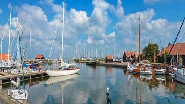 Un port de plaisance où sont amarrés de nombreux voiliers, entouré d’immeubles aux toits rouges.