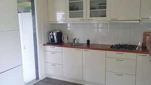 Une cuisine avec des meubles blancs, une machine à café, une bouilloire et une cuisinière à gaz.