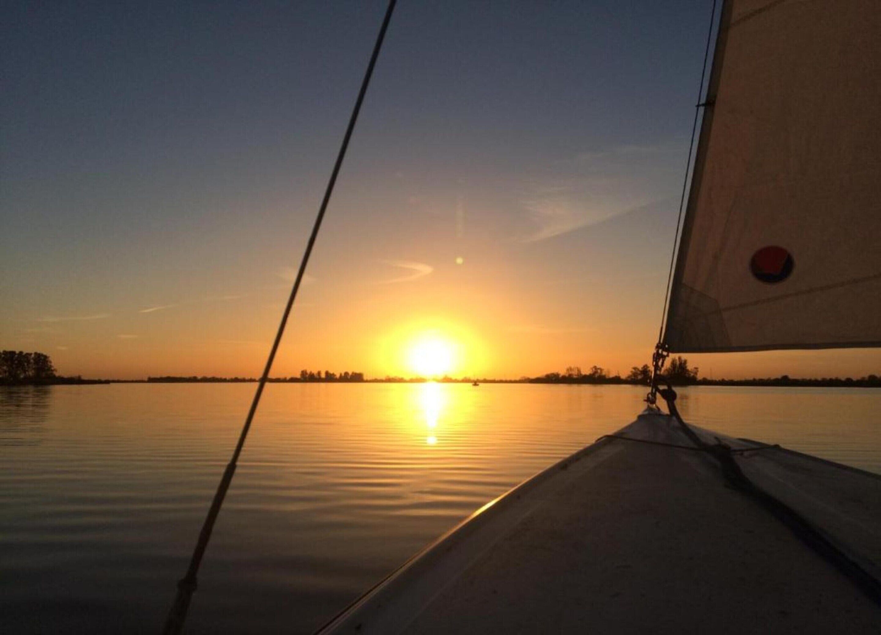 A sunset over a calm body of water with a sailboat's mast and rigging in the foreground.