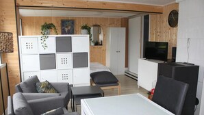 A modern living room with a sofa, coffee table, and a TV. There is a white cabinet with storage, a wooden wall, and a clock. - Cozy Family Duplex on the Belgian Coast (Middelkerke)