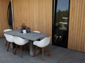 A modern outdoor dining area with a concrete table and white chairs, a coffee pot, and decorative vases. - Villa on the Water Near the Veluwemeer (Zeewolde)