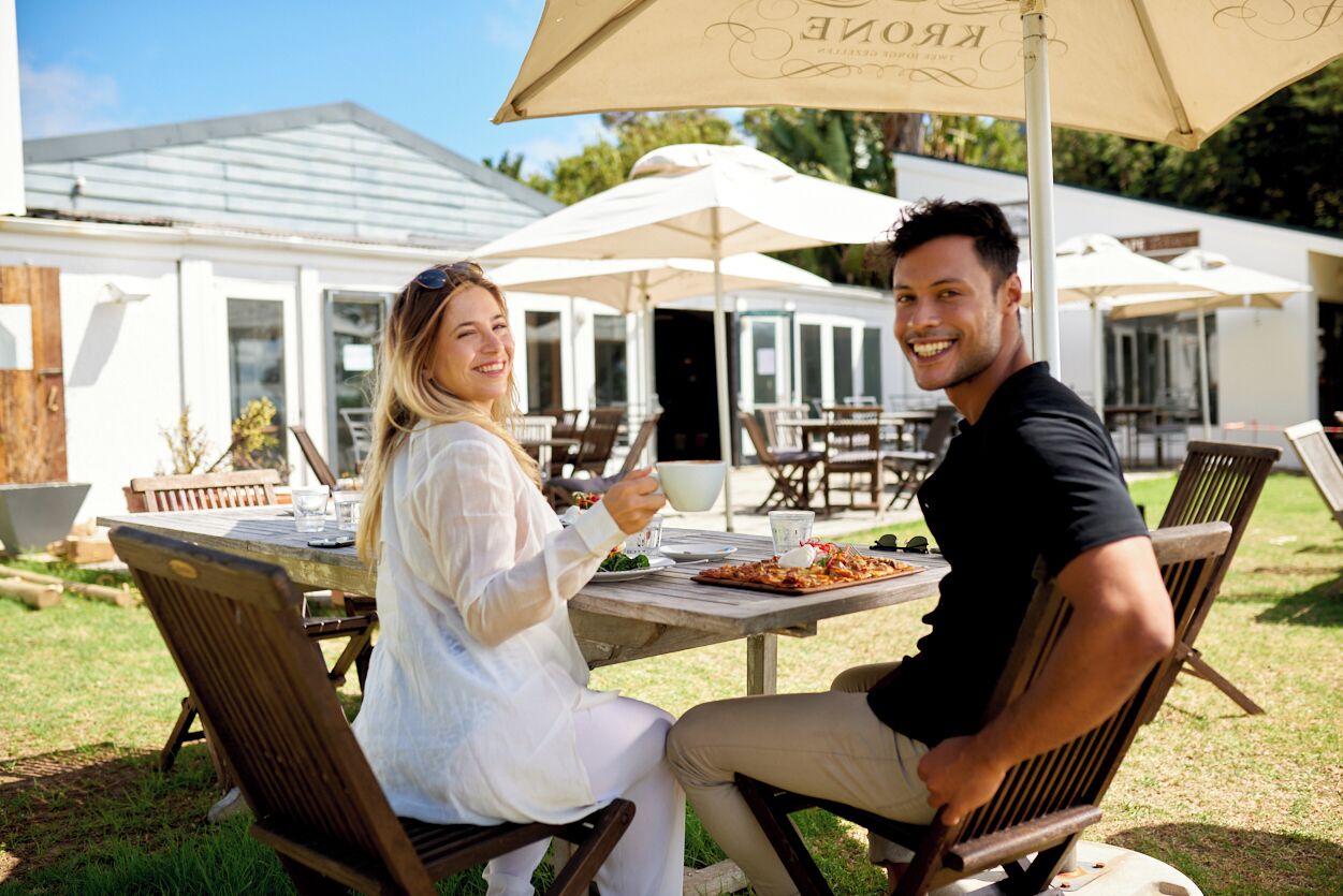 Two people seated at an outdoor table with a pizza, under a large umbrella.