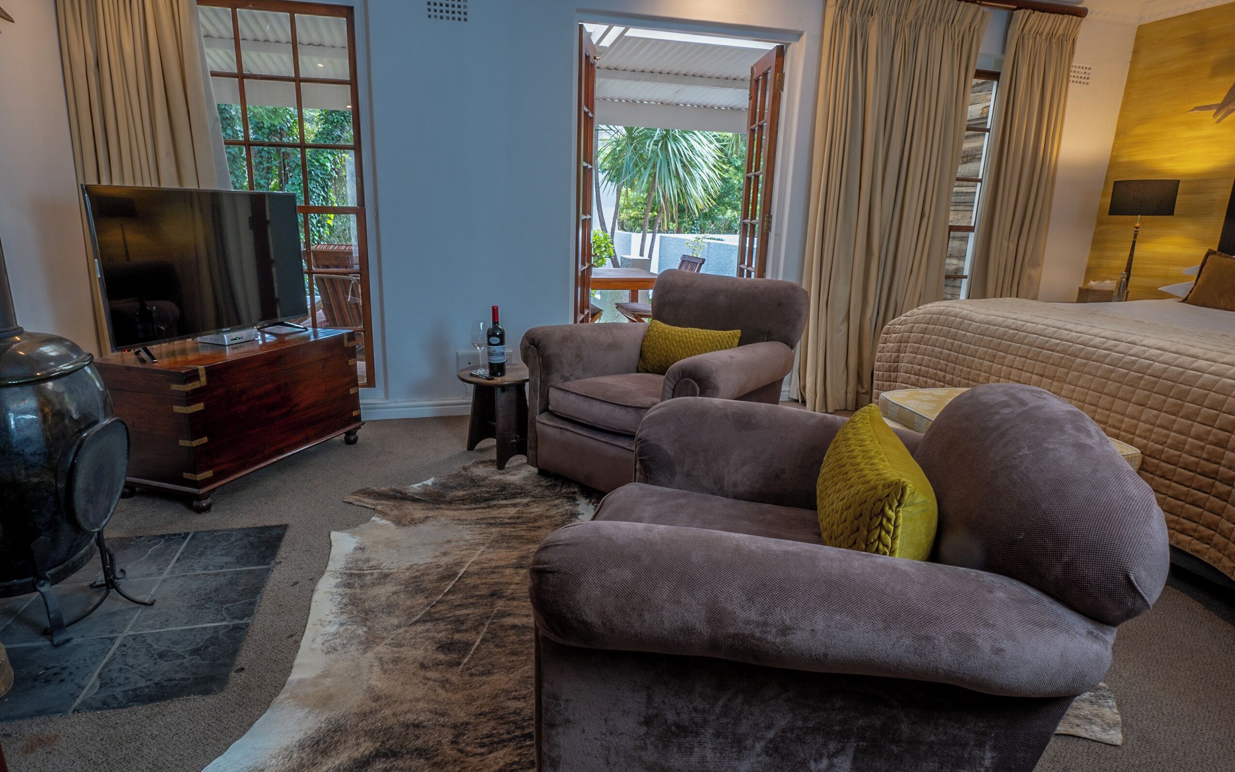 A modern living room with a large bed, a sofa, a TV, and a small table with a bottle of wine.