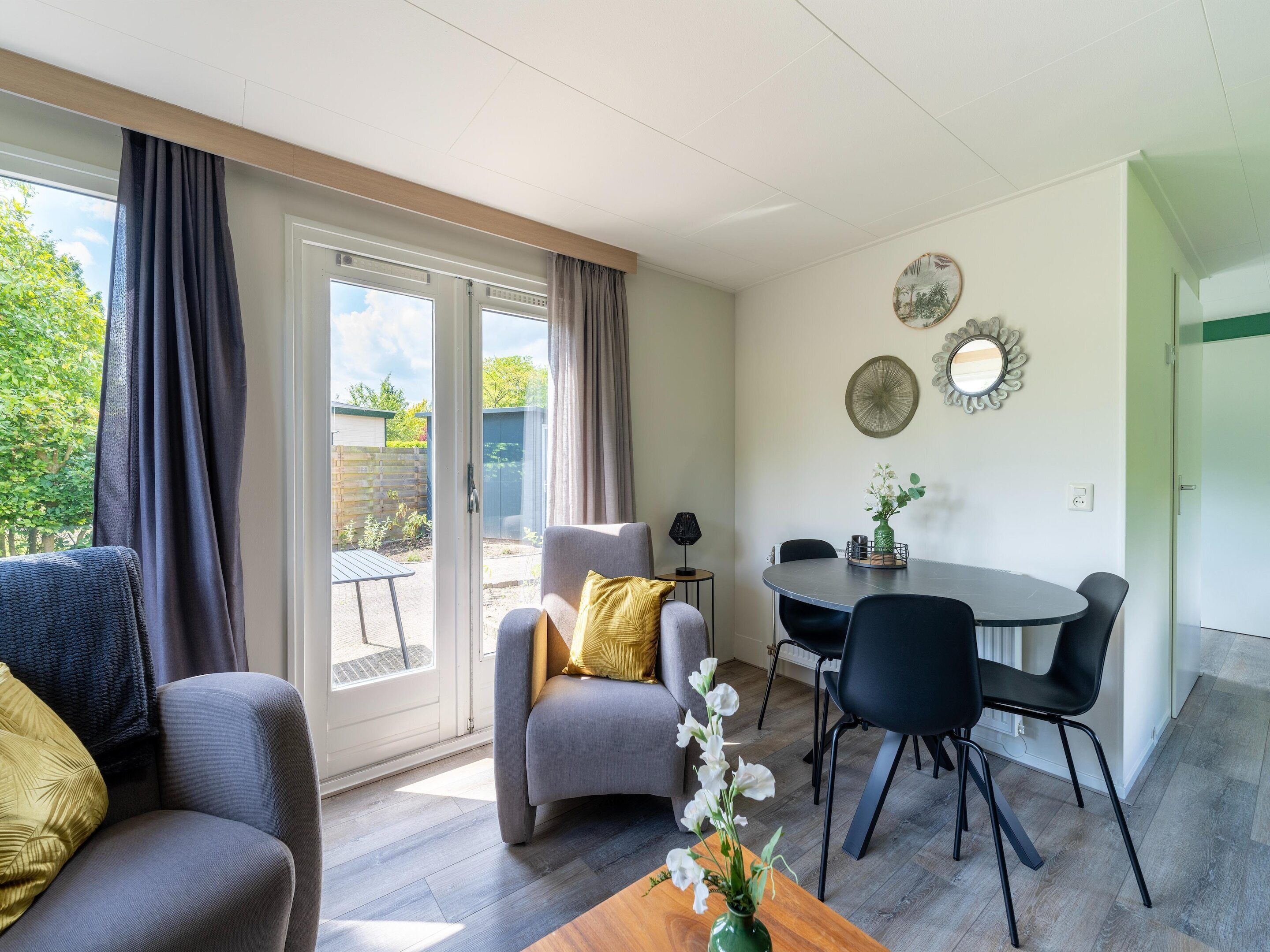 Ein modernes Wohnzimmer mit einer Couch, einem Esstisch mit Stühlen und Blick durch eine Schiebetür auf einen Außenbereich.