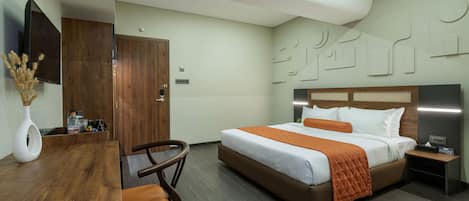 Una habitación de hotel con un escritorio de madera, una cama con una manta naranja, una mesita de noche y un televisor montado en la pared.
