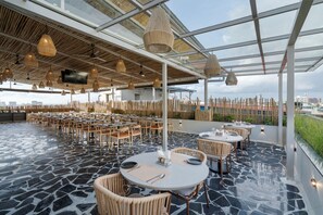 A rooftop dining area with round tables, wicker chairs, and a TV screen. - Fressotel, Kanakapura Road (Bengaluru)
