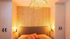 A bedroom with a wooden slat wall, a bed with an orange bedspread, and two wall-mounted lamps. - Luxury Chalet in Stegeren, Beautiful Surroundings (Stegeren)