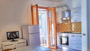A compact kitchen with a refrigerator, stove, oven, and a small television on a cabinet. - Cosy Apartment 200m From the sea (Ravenna)