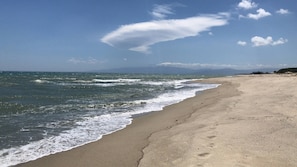 A beach with waves, a clear sky, and distant mountains.