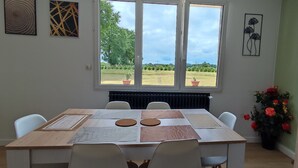 Zona de menjador amb una taula preparada per a quatre persones, un radiador i vista al jardí a través de grans finestres.