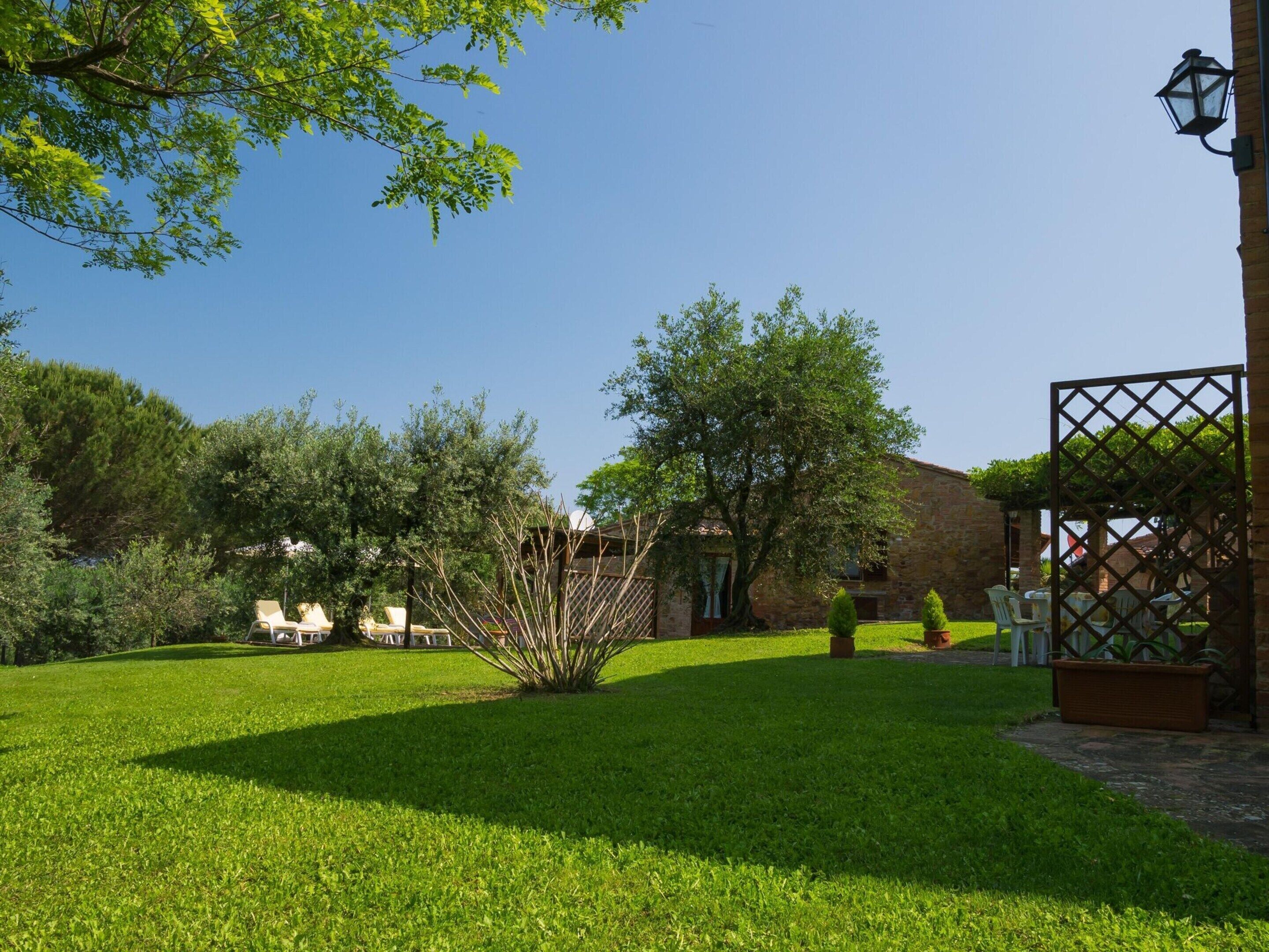 A well-maintained garden with a stone building, a pergola, and outdoor seating.
