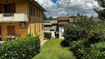 A yellow building with a balcony, a small garden, and a clear sky.