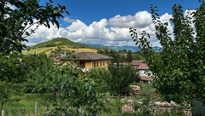 A rural landscape with a yellow house surrounded by greenery and hills.