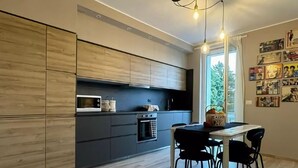 A modern kitchen with dark cabinets, a microwave, and a stove. There is a dining table with chairs and a window with a view of greenery.