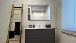 A bathroom with a marble wall, a wooden ladder, a dark vanity with a mirror, and a window.