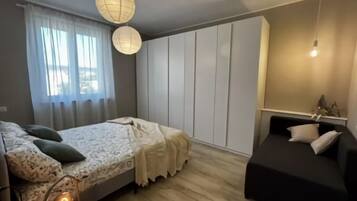A bedroom with a bed, bedside table, lamp, and a black sofa.