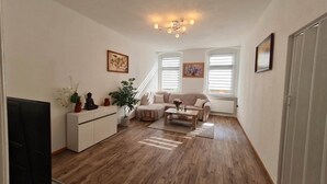 Ένα σαλόνι με έναν καναπέ, ένα τραπεζάκι και μια τηλεόραση. Υπάρχει μια σκάλα που οδηγεί σε ένα άλλο επίπεδο.