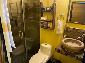 Een badkamer met een douchecabine van glas, een toilet, een wastafel met een rond bassin en een plank met toiletartikelen.