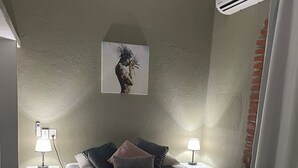 A bedroom with a bed, two bedside tables with lamps, a wall-mounted air conditioner, and a painting. - Centrally located apartment  (Puerto Vallarta)