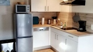 Una cocina compacta con armarios blancos, un refrigerador de acero inoxidable, un microondas y un lavamanos.
