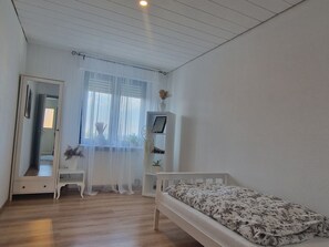A bedroom with a bed, a bedside table, a mirror, a window with sheer curtains, and a shelf with decorative items. - Wohnung im Teutoburger Wald Externsteine (Nieheim)