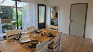 A dining area with a wooden table set for four, white chairs, and a view of a garden through large windows. - Wohnung im Teutoburger Wald Externsteine (Nieheim)