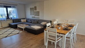 A modern living room with a sofa set, a dining table with chairs, and a white brick wall with abstract art. - Wohnung im Teutoburger Wald Externsteine (Nieheim)