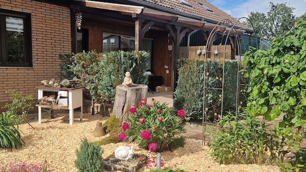 A garden with a variety of plants and flowers, a wooden bench, and a statue. - Wohnung im Teutoburger Wald Externsteine (Nieheim)