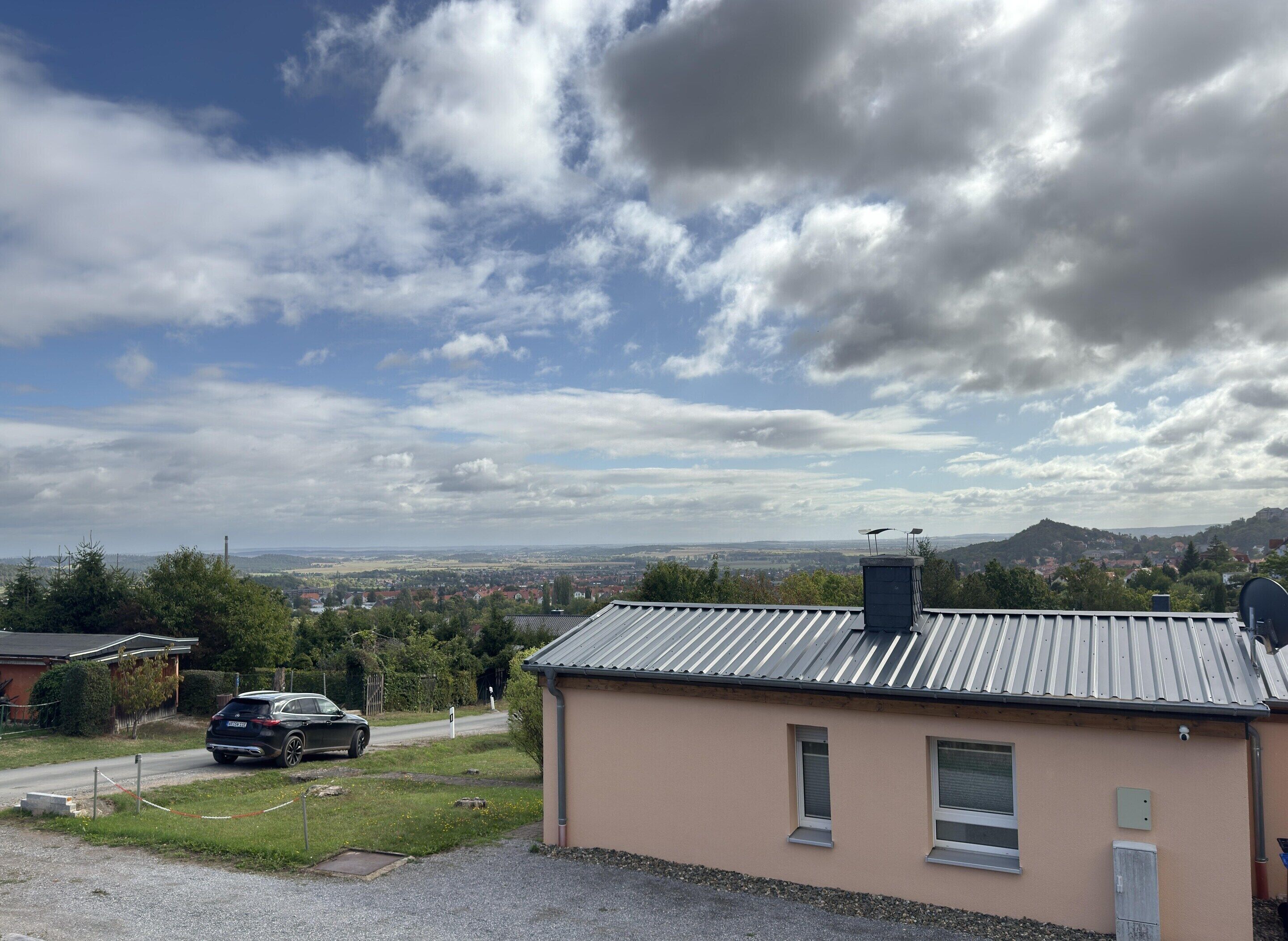 Un bâtiment doté d’un toit en métal, d’une antenne parabolique et offrant une vue sur un paysage lointain, avec des collines et une route.