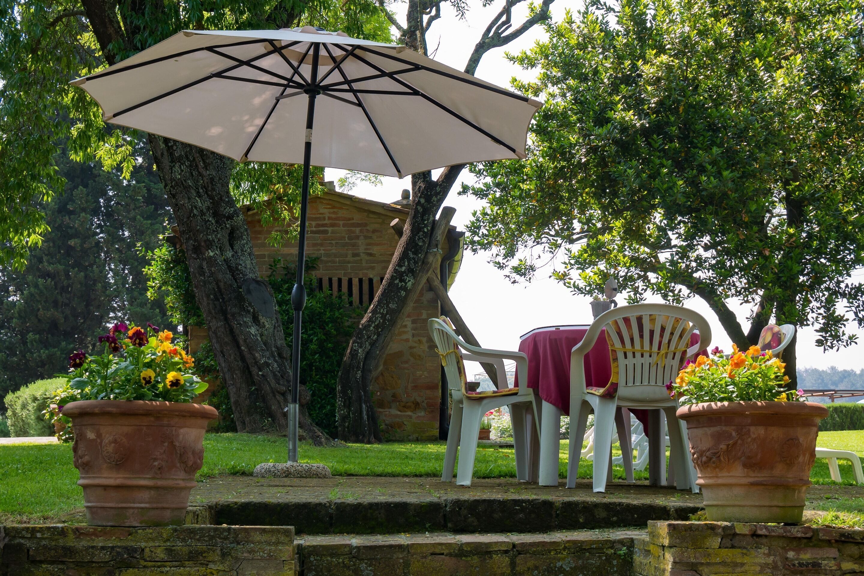 An outdoor seating area with a table and chairs, a large umbrella, and potted plants.