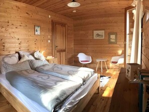 A wooden cabin room with a bed, two chairs, a small table, and a door leading outside. - The Karl Anton Hutte (Ferlach)
