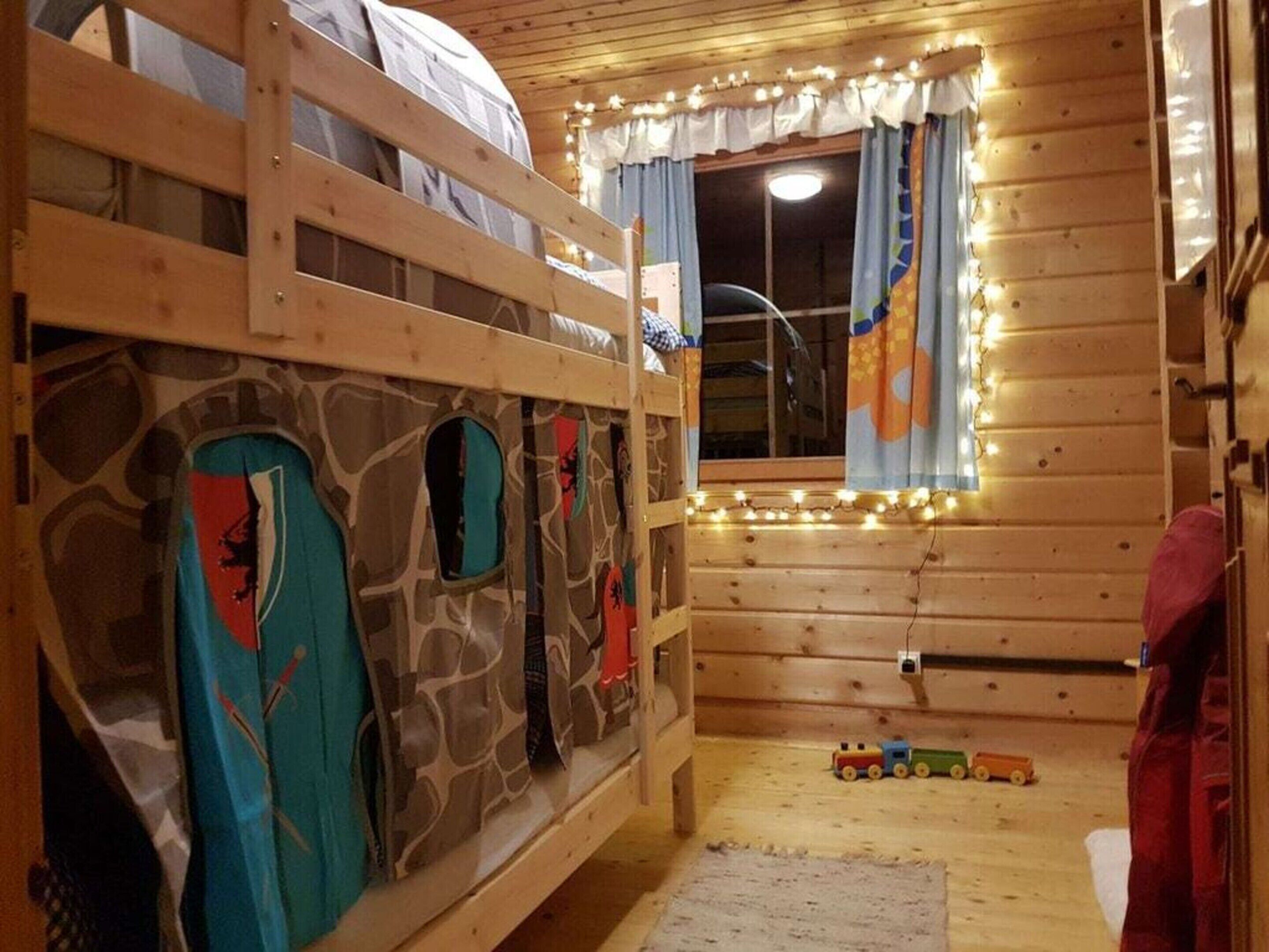 A cozy cabin with bunk beds, a window with curtains, and a toy train on the floor.