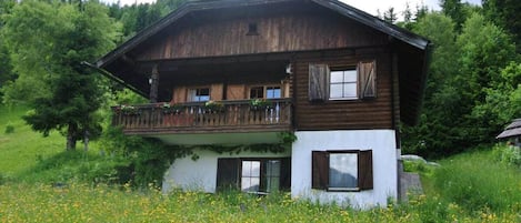 A traditional wooden chalet with a balcony, surrounded by a lush green field.